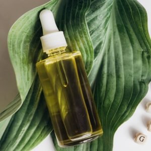 A bottle of natural skincare oil placed on green leaves with letter blocks spelling out 'morning'.